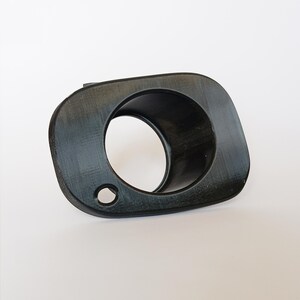 May include: A black, 3D-printed plastic part with a rounded rectangular shape and a central circular opening. A smaller hole is visible near the edge. The object has a textured surface and appears to be a component of a larger assembly.