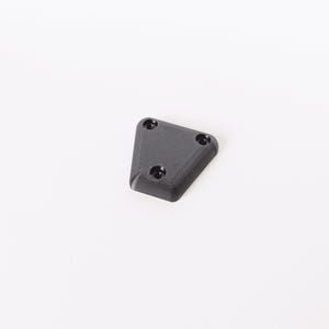 May include: A small, black, triangular object with three circular holes. The object has a slightly textured surface and appears to be made of plastic or a similar material. The item is set against a plain white background.