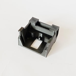 Puede incluir: Una carcasa de plástico negra impresa en 3D con una abertura rectangular. La carcasa tiene un borde elevado alrededor de la abertura.
