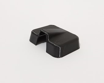 Puede incluir: Un tope de puerta de plástico negro con una parte superior curva y una base rectangular. El tope de puerta tiene una pequeña abertura en el centro.