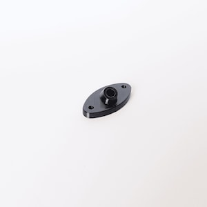 May include: A black, oval component featuring a central raised cylinder and two small holes. The part is made of a solid, dark material, likely a small mechanical fitting or component.