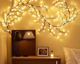 May include: A bedroom scene with a cosy atmosphere. Branch-shaped string lights with warm white bulbs are arranged on the wall. A wooden bedside table supports lamps, a framed picture, and a small bottle, creating a soft glow.