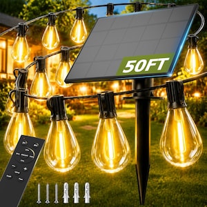 May include: A string of outdoor solar-powered LED string lights with clear teardrop-shaped bulbs emitting a warm glow. The set includes a black solar panel labeled 50FT, a remote control with brightness settings, and mounting hardware.