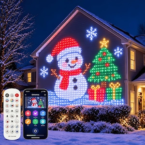 May include: A grid of LED lights projected onto a house exterior displaying a snowman, a Christmas tree, and gifts. A white remote control and a smartphone showing a control app interface are positioned in the foreground for scale.