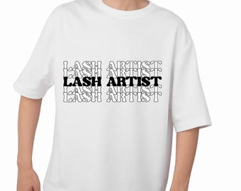 May include: White t-shirt with the text "LASH ARTIST" in a stacked, repeating design. The text is black with a white outline, creating a layered effect. The shirt has short sleeves and a relaxed fit.