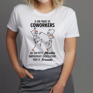 Puede incluir: Camiseta blanca con el texto "A JOB MADE US COWORKERS" sobre un gráfico de dos esqueletos bailando. El texto "BUT OUR POTTY MOUTHS INAPPROPRIATE CONVERSATIONS MADE US FRIENDS" está debajo. Los esqueletos tienen acentos naranjas y marrones.