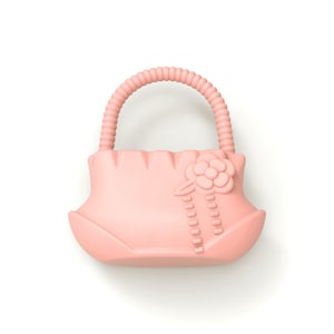 May include: A light pink purse-shaped teether with a textured handle and a flower detail. The teether has a ridged handle and a decorative flower on the front. The overall design is soft and rounded, suitable for babies.