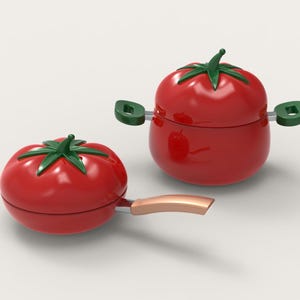 Könnte beinhalten: Zwei rote, tomatenförmige Küchenartikel: ein kleiner Topf mit grünen Griffen und eine Bratpfanne mit kupferfarbenem Griff. Beide haben grüne, blattartige Oberteile. Auf weißem Hintergrund.