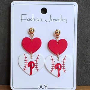 Könnte beinhalten: Fashion Jewelry Ohrringe mit einem roten Herz und einem Baseball-Herzen mit rotem "P". Die Ohrringe sind auf einer weißen Karte mit dem Text "Fashion Jewelry" und den Initialen "A.Y."