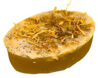 May include: A golden yellow soap bar with a swirl of white and a layer of dried orange petals on top.