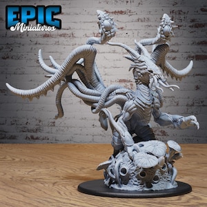 May include: A light gray resin miniature figure of a multi-headed creature with numerous tentacles, horns, and a central body structure, standing on a base decorated with mushroom-like growths and circular textures, presented in a neutral matte finish.