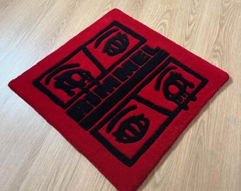 Puede incluir: Una alfombra cuadrada roja con un diseño negro y la palabra "RIMMEL" en el centro. La alfombra tiene un patrón geométrico con formas estilizadas en cada esquina. La alfombra está colocada sobre un suelo de madera clara.