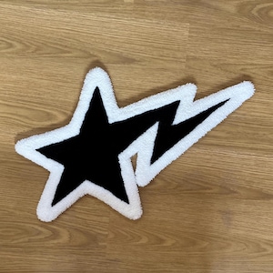 Puede incluir: Una alfombra negra y blanca con un diseño de estrella y rayo. La alfombra está hecha de un material esponjoso.