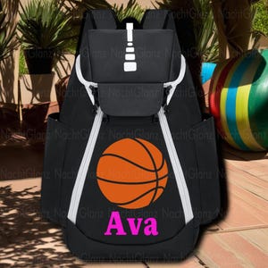 May include: Black backpack with white accents and a basketball graphic. The backpack has a large orange basketball design and the name "Ava" in pink. Features include side pockets and a top handle.