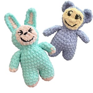 May include: Two handmade crochet stuffed animals: a turquoise bunny and a lavender monkey. The bunny has long ears and pink accents on its face, feet, and ears. The monkey has a smiling face and is holding its arms out. Both toys have black embroidered facial features.