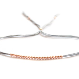 May include: A gray string bracelet with a row of small gold beads.