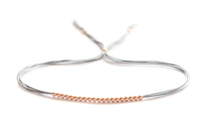 May include: A gray string bracelet with a row of small gold beads.