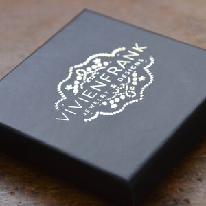 May include: A black box with a silver logo that reads "VIVIEN FRANK JEWELRY & DESIGNS".