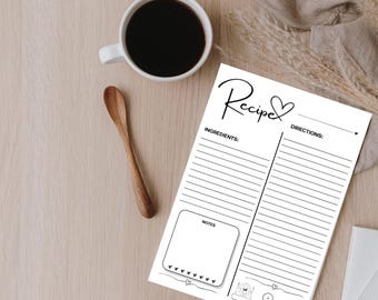 May include: A recipe notepad with the word "Recipe" in cursive, a coffee cup, and a wooden spoon rest on a light wood surface. The notepad has sections for ingredients, directions, and notes, with small icons at the bottom.