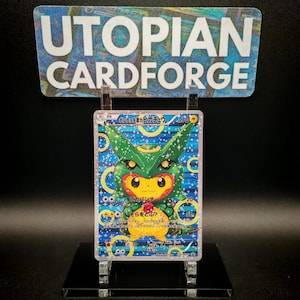 May include: A Pokémon trading card featuring a Pikachu character wearing a green costume with yellow accents. The card has Japanese text and is displayed on a clear stand. The sign above the card reads "UTOPIAN CARDFORGE".