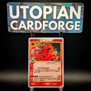 May include: A Pokémon trading card featuring a red Gyarados illustration with Japanese text. The card has a HP of 80 and includes the text "Spiral Glow" and "Finish Burn". The card is displayed in front of a sign that reads "UTOPIAN CARDFORGE".
