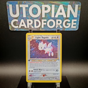 Könnte beinhalten: Eine Light Togetic Pokémon-Karte aus dem Pokémon Sammelkartenspiel. Die Karte ist gelb mit einem blauen Rand und zeigt eine Illustration eines weißen Light Togetic Pokémon mit rosa Akzenten. Der Kartentext lautet "Light Togetic" und "Glücks-Pokémon. Länge: 2'0", Gewicht: 7 lbs."