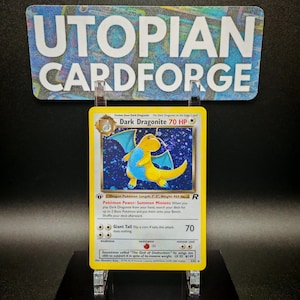 Könnte beinhalten: Eine gelbe und blaue Dark Dragonite Pokémon-Karte aus dem Sammelkartenspiel von Wizards of the Coast. Die Karte zeigt einen gelben Drachen mit blauen Flügeln und einem blauen Schwanz. Die Karte stammt aus dem Fossil-Set und hat 70 KP.