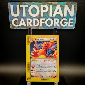 May include: A Charizard Pokémon card with a yellow border, featuring an orange dragon illustration. The card displays the text "Charizard 110 HP" and "Fireblast" with attack details. The card is displayed in front of a sign that says "UTOPIAN CARDFORGE".