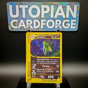 Könnte beinhalten: Eine Tyranitar-Pokémon-Karte aus dem Pokémon Sammelkartenspiel. Die Karte ist gelb mit schwarzem Rand und zeigt ein grünes Tyranitar-Pokémon vor einem violetten Hintergrund. Die Karte hat einen KP-Wert von 120 und die Texte "Zerstörerisches Brüllen", "Schwanzschlagen" und "Gigaknacker" sind sichtbar.