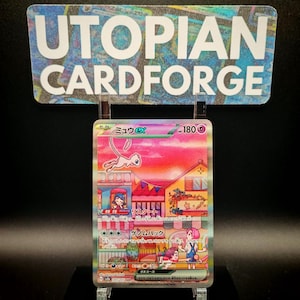 May include: A holographic trading card featuring a pink Mew EX character over a colorful cityscape. The card has Japanese text and a 180 HP indicator. The card is displayed on a clear stand with a sign that reads "UTOPIAN CARDFORGE".