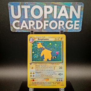 Könnte beinhalten: Ampharos Pokémon-Karte aus dem Wizards of the Coast Sammelkartenspiel. Die Karte ist eine Stufe-2-Karte und zeigt ein gelbes Ampharos-Pokémon mit einem rosa Schwanz. Die Karte hat einen hellblauen Hintergrund mit einem holografischen Effekt. Die Karte hat einen Wert von 90 KP und die Texte "Attract Current" und "Gigavolt" sind sichtbar.