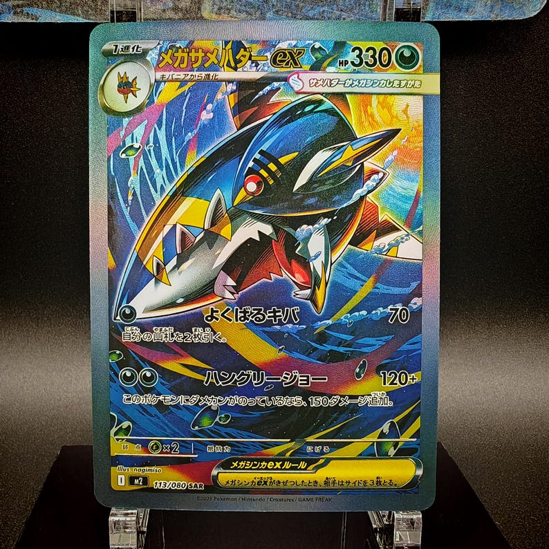 May include: A holographic Pok&eacute;mon trading card featuring a Mega Sharpedo EX. The card has a blue, red, and yellow color scheme with Japanese text. The card is displayed on a clear stand.