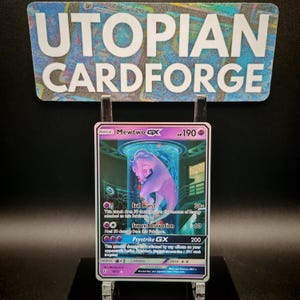 Puede incluir: Una carta coleccionable Mewtwo GX, con tonos morados y azules. Presenta una imagen holográfica de Mewtwo dentro de un tubo. El texto "UTOPIAN CARDFORGE" es visible en la parte superior.