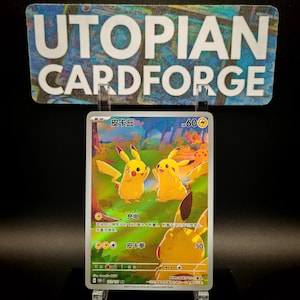 May include: A Pokémon trading card featuring Pikachu characters in a forest scene. The card has Japanese text and a 60 power rating. The card is displayed in a clear acrylic holder with a sign that reads "UTOPIAN CARDFORGE" in white letters.