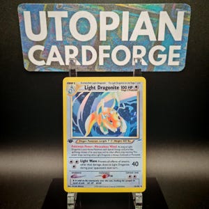 Könnte beinhalten: Eine Light Dragonite Pokémon-Karte mit gelbem Rand. Die Karte zeigt eine farbenfrohe Illustration eines drachenartigen Wesens. Der Text "Light Dragonite 100 HP" ist sichtbar. Die Karte wird in einem transparenten Halter präsentiert.