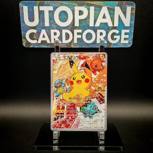 May include: A Pokemon trading card featuring Pikachu and other characters. The card has Japanese text and is displayed on a clear stand. The card is from Utopian Cardforge.