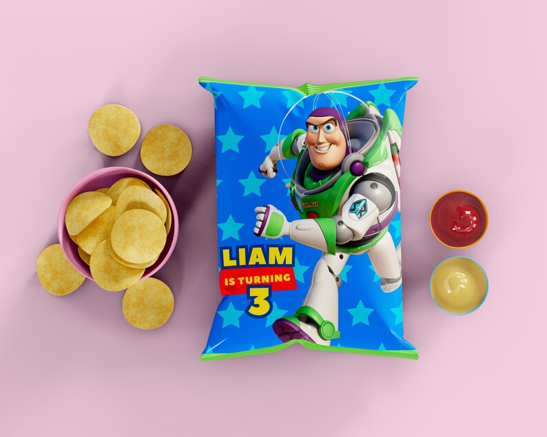 Puede incluir: Una bolsa de patatas fritas azul con Buzz Lightyear de Toy Story, con el texto "LIAM IS TURNING 3". La bolsa est&aacute; rodeada de patatas fritas en un cuenco rosa, patatas fritas sueltas y peque&ntilde;os cuencos con salsas rojas y amarillas. El fondo es rosa liso.