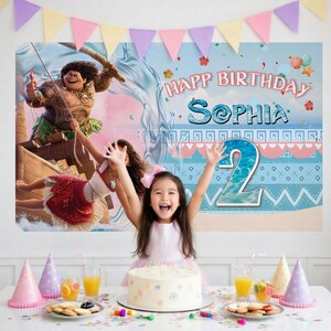 May include: A birthday party backdrop featuring Moana and Maui characters, the text "HAPP BIRTHDAY SOPHIA" and a large number "2". The scene includes a light blue background with ocean waves, a sandy beach, and colorful triangular bunting flags.