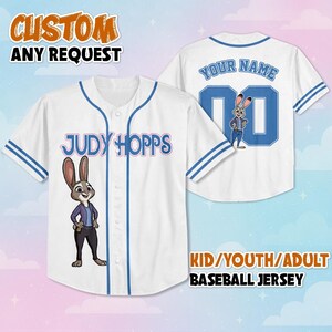 May include: A white baseball jersey with blue trim, featuring a graphic of Judy Hopps on the front and the text Judy Hopps. The back displays the text Your Name, the number 00, and a graphic of Judy Hopps. The jersey has a button-down front.