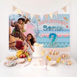 May include: A birthday party backdrop featuring Moana and Maui characters, the text "HAPP BIRTHDAY SOPHIA" and a large number "2". The table includes a white cake, plates of cookies, cupcakes, fruit, and glasses of orange juice with a banner above.
