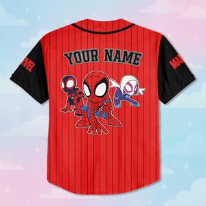 Puede incluir: Camiseta de b&eacute;isbol roja y negra con el texto "YOUR NAME" en la espalda. La camiseta presenta un gr&aacute;fico de dibujos animados de Spider-Man y otros dos personajes de Spider-Verse. Las mangas son negras con la palabra "MARVEL" impresa en la manga izquierda.