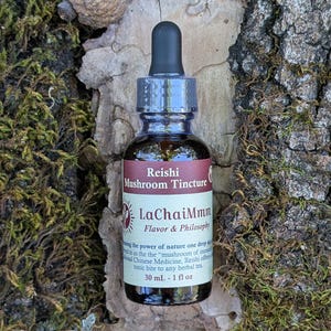 May include: A small glass bottle of Reishi Mushroom Tincture with a black dropper. The label reads "LaChaiMmm Flavor & Philosophy" and "30 mL - 1 fl oz". The bottle sits on a bed of leaves, moss, and bark, with an acorn in the background.