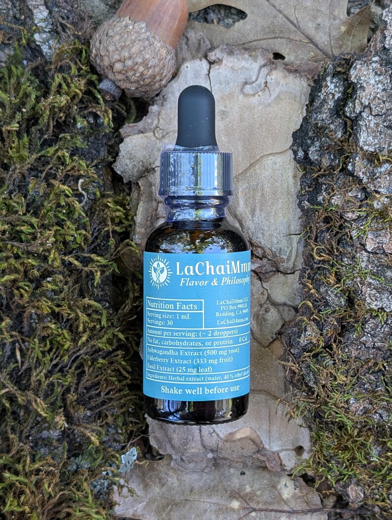 May include: A small, dark glass bottle with a black dropper top, labeled "LaChaiMm Flavor & Philosophy." The label includes nutrition facts and ingredient information. The bottle is surrounded by moss, leaves, and an acorn.