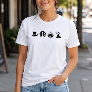 May include: A white short-sleeve t-shirt featuring a horizontal row of four black graphic icons centered on the chest. The icons depict a sailing ship, a trident inside a circle, a stylized mountain or wave shape, and a figure sitting on a rock.