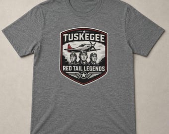 Może przedstawiać: Szary melanżowy t-shirt z krótkim rękawem i centralną grafiką w kształcie tarczy. Wzór zawiera napis TUSKEGEE i RED TAIL LEGENDS, ilustrację samolotu śmigłowego oraz trzech pilotów w hełmach lotniczych i goglach.