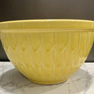 Puede incluir: Un gran cuenco de cerámica amarilla con un patrón decorativo texturizado. El cuenco tiene un borde ancho y una forma redondeada, adecuado para hornear y preparar alimentos.