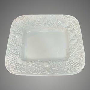 May include: A square white ceramic serving dish featuring a raised, embossed border design of textured pinecones, acorns, and oak leaves. The center of the dish is smooth and recessed, while the rim displays a detailed, three-dimensional botanical pattern that wraps around all four sides of the piece.