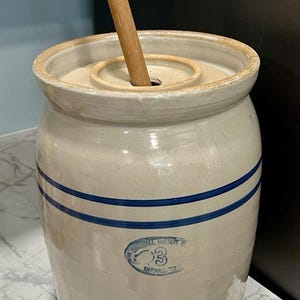 Peut inclure: Un barattage à beurre en grès vintage avec une palette en bois. Le barattage est blanc cassé avec deux rayures bleues et un tampon bleu qui dit "Marshall Pottery 3". Un article de cuisine classique.