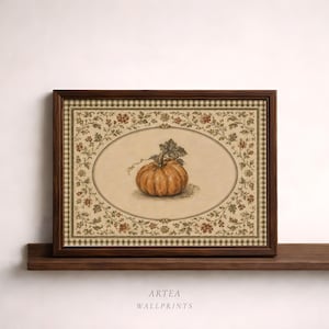 May include: A framed wall print featuring a central illustration of an orange pumpkin inside an oval border. The background is cream-colored with a decorative floral vine pattern and a brown checkered border. The text ARTEA WALLPRINTS is below.