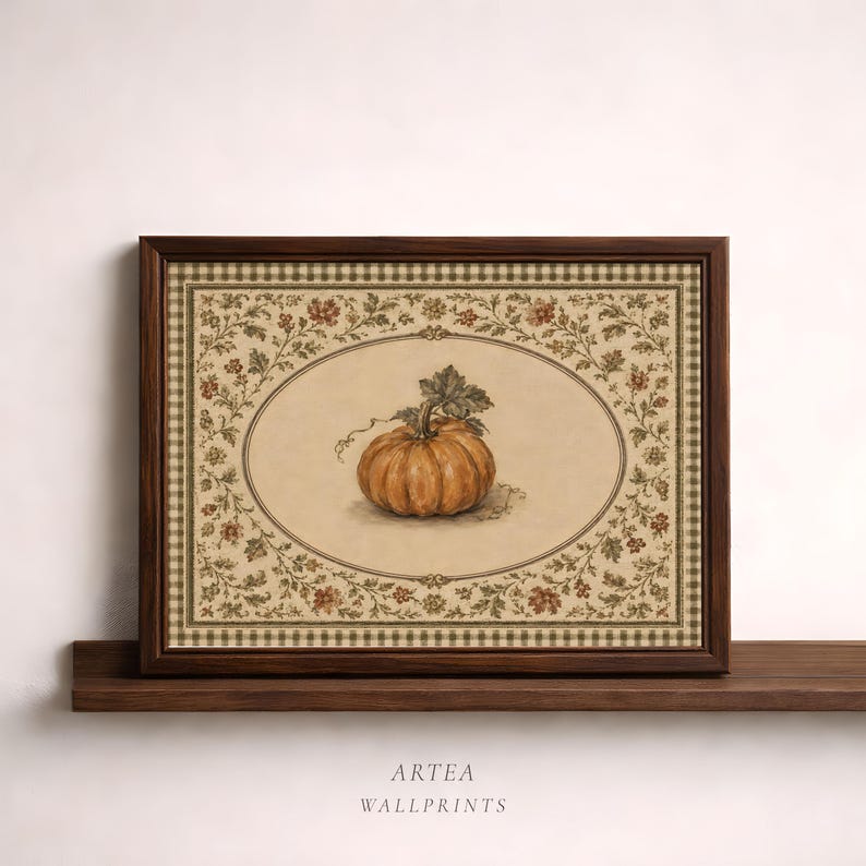 May include: A framed wall print featuring a central illustration of an orange pumpkin inside an oval border. The background is cream-colored with a decorative floral vine pattern and a brown checkered border. The text ARTEA WALLPRINTS is below.